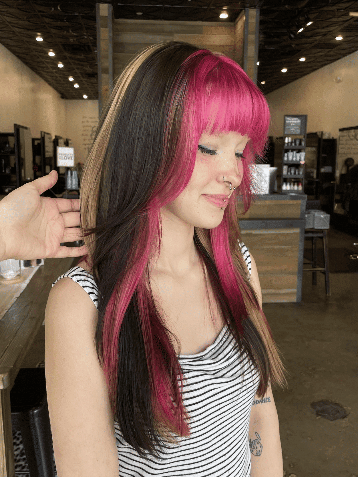 Young woman with vibrant pink and dark hair, smiling in a salon.