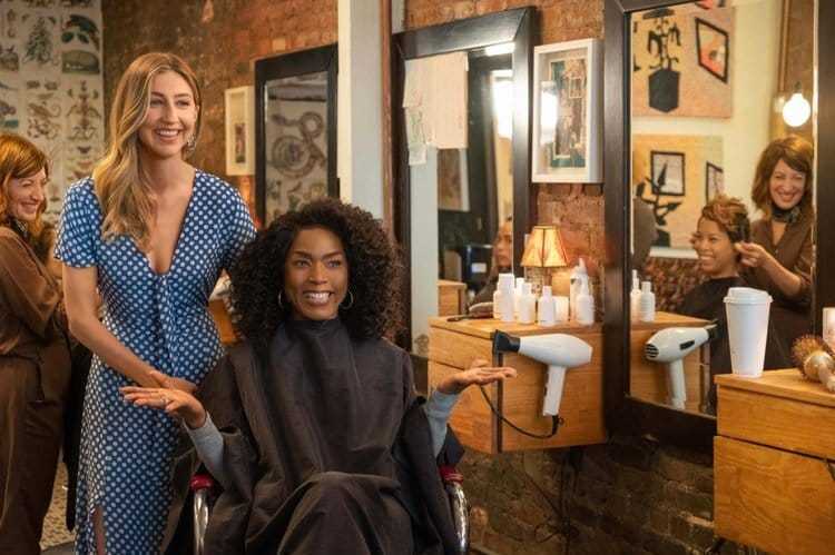 Two women smiling at a hair salon, one seated with a fresh hairstyle, others chatting in the background.